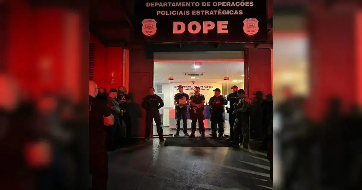 Grupo de pessoas em frente ao Departamento de Operações Policiais Estratégicas, com iluminação vermelha.