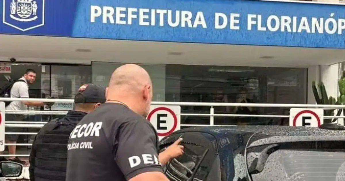 Placa da Prefeitura de Florianópolis ao fundo, com pessoas e policiais civis em primeiro plano.