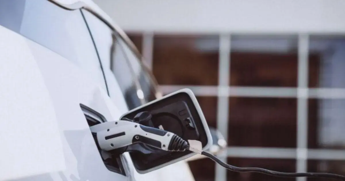 Porta de carregamento de um carro elétrico com cabo conectado, em fundo de claridade.