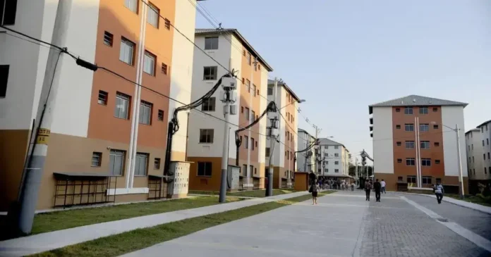 Conjunto habitacional com prédios de diferentes cores em uma área aberta, com pessoas caminhando na via.