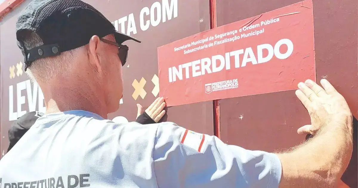Homem colocando um aviso de interdição em uma parede, com texto legível informando 