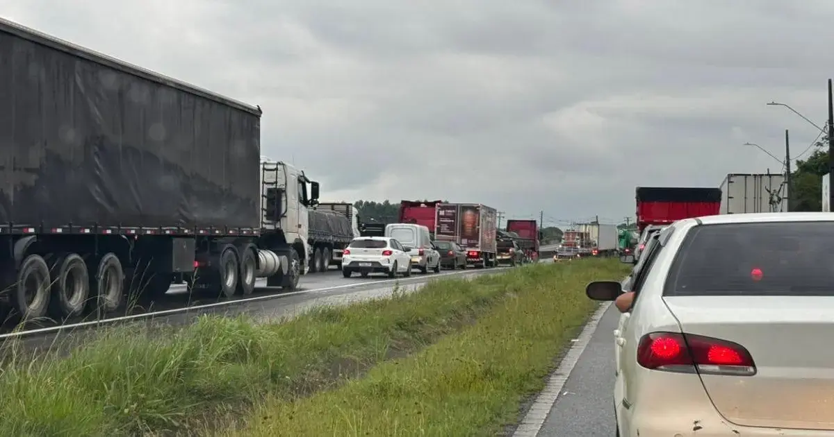 Congestionamento com diversos caminhões e carros em uma rodovia sob céu nublado.