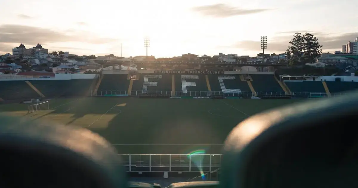 Estádio vazio do Figueirense Futebol Clube ao entardecer, com iluminação e gramado visíveis.