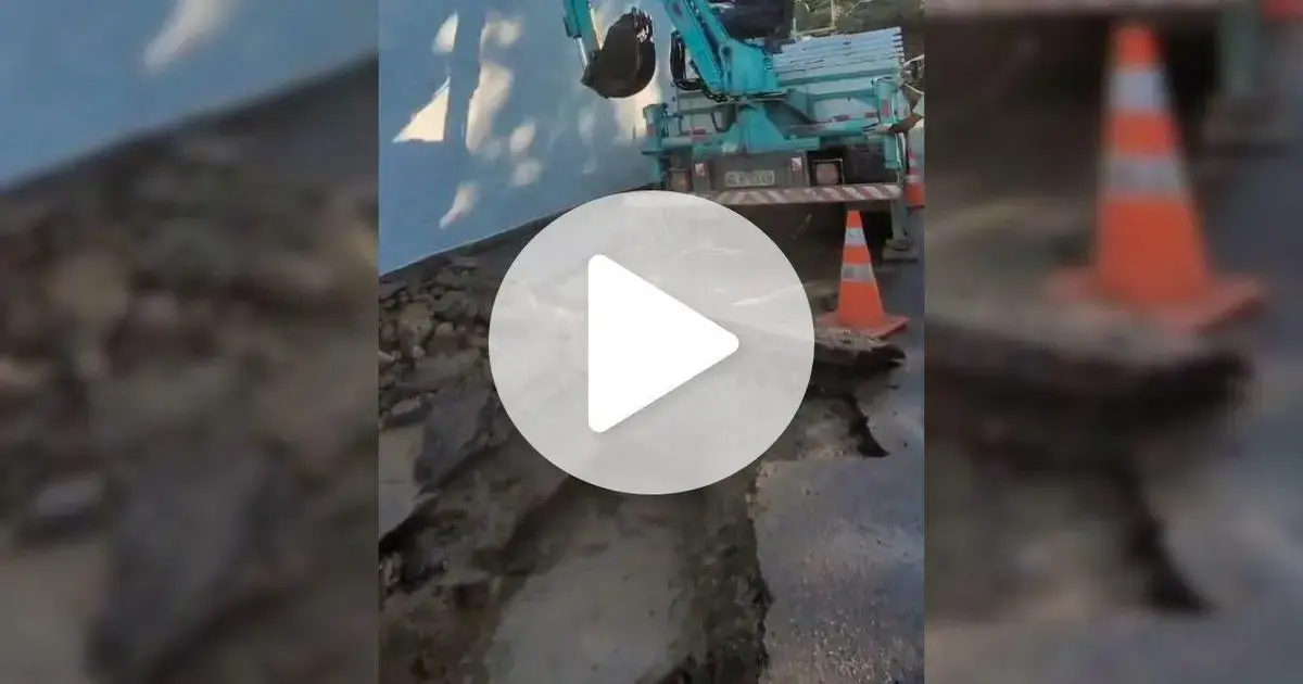 Veículo de trabalho próximo a um buraco na pista, com cones de sinalização ao redor.