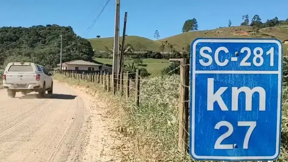 Placa indicativa do quilômetro 2,7 da rodovia SC-281, com vegetação e uma casa ao fundo.