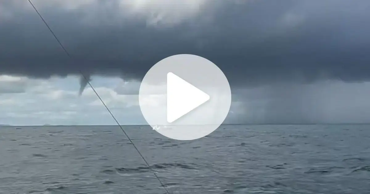Um fenômeno meteorológico em alto-mar, com nuvens escuras e uma tromba d'água visível ao fundo.