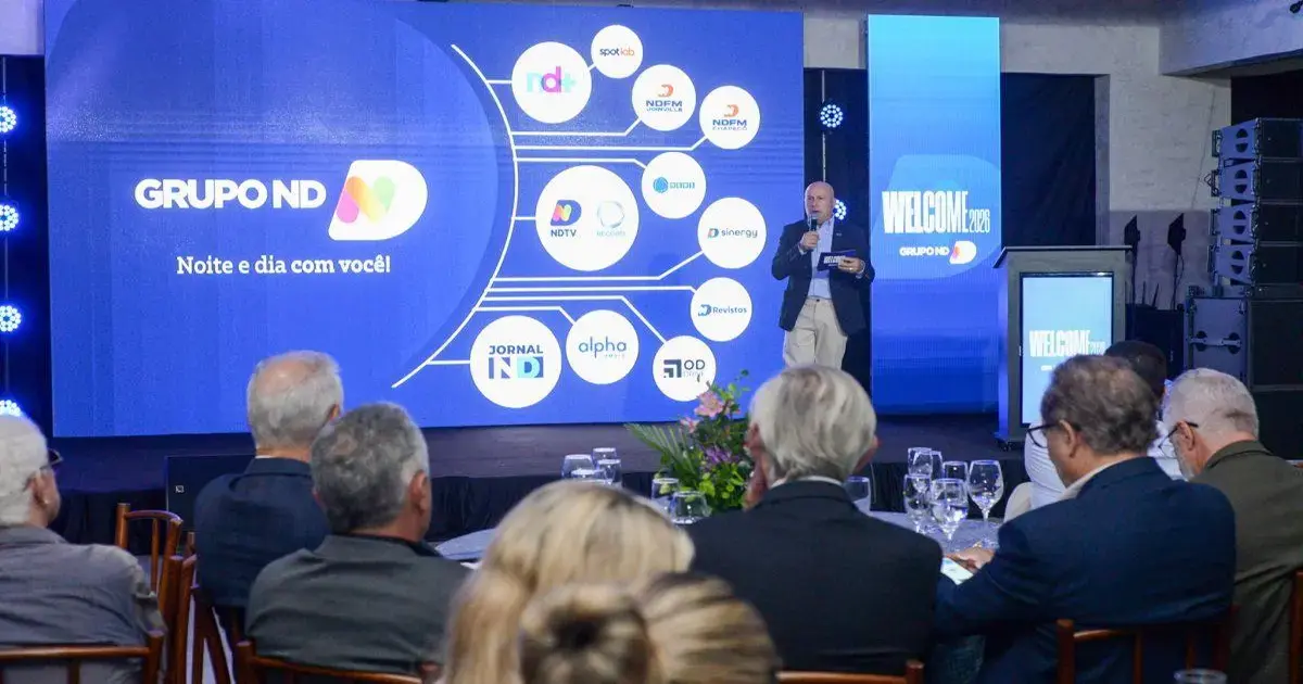 Evento do Grupo ND com apresentações em um palco, exibição de logotipos e público ao fundo.