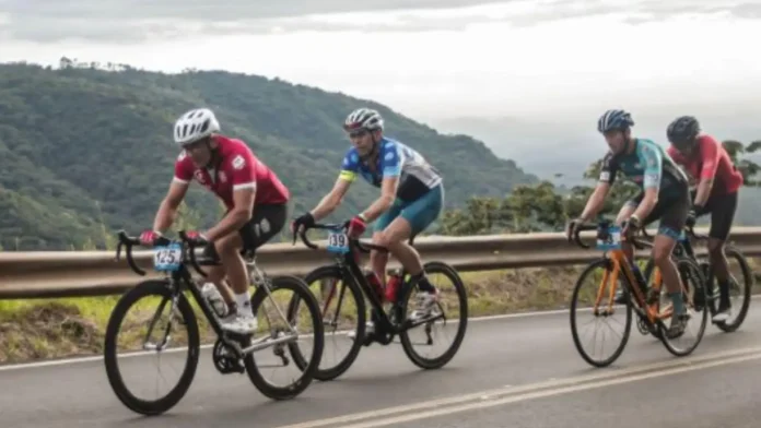 Ciclístas em uma estrada, pedalando em um trecho montanhoso, durante uma competição de ciclismo.