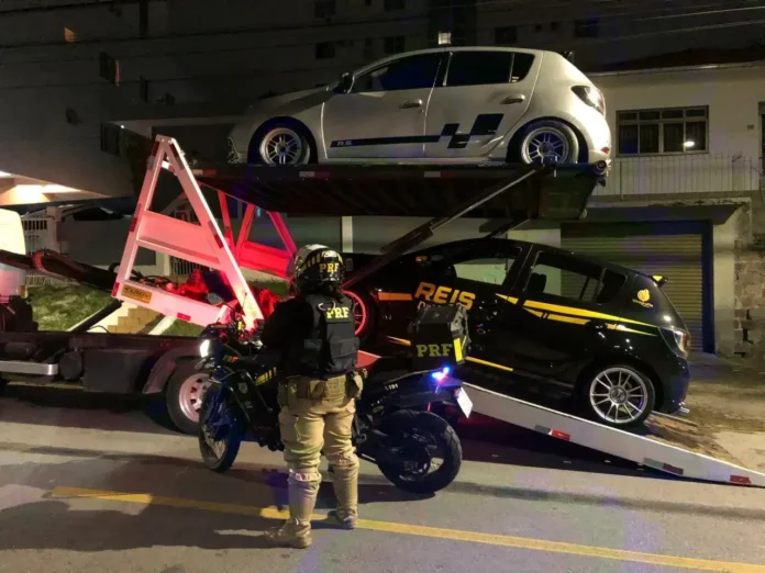 Veículo da Polícia Rodoviária Federal com dois carros em um reboque, um em cima e outro embaixo.