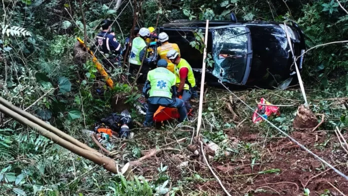 Equipes de resgate auxiliam vítimas em um carro acidentado em uma ribanceira cercada por vegetação.