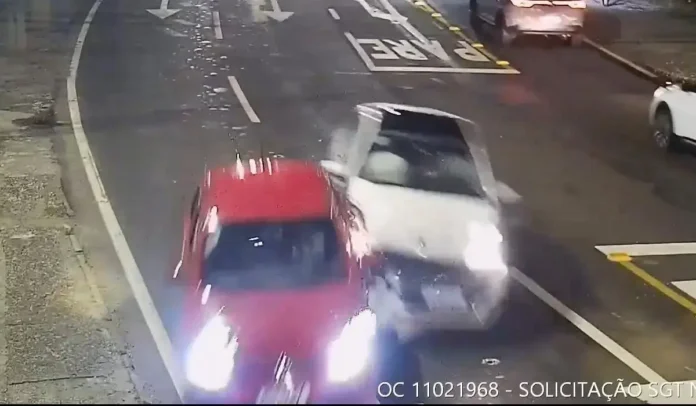 Colisão entre um carro vermelho e um carro branco em uma rua, à noite.