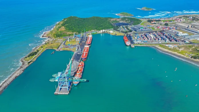 Vista aérea do Porto de Imbituba, com navios cargueiros atracados e contêineres ao fundo.