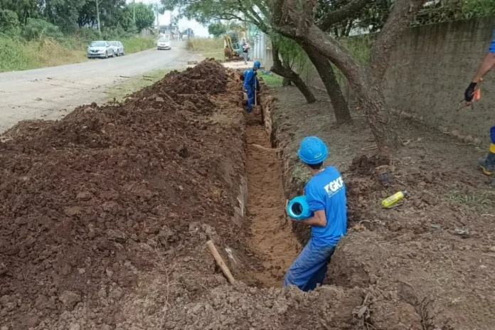 Trabalho em equipe realizando escavação em trench na beira da estrada para instalação de tubulação.