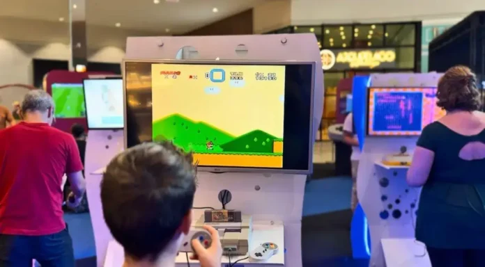 Tela de videogame exibindo jogo de plataforma com personagens e cenário colorido, enquanto jogadores interagem com consoles.