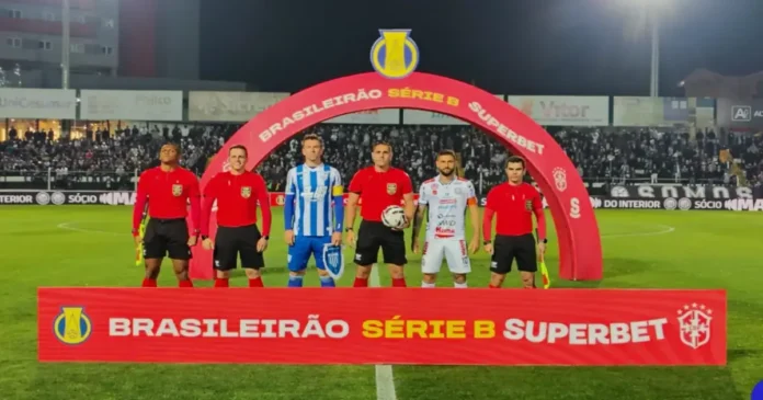 Jogadores e árbitros em campo sob um arco com a inscrição "Brasileirão Série B Superbet", em partida de futebol.