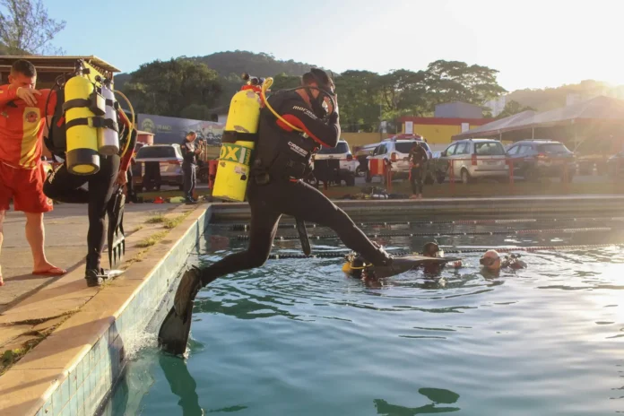 Mergulhador saltando na piscina durante treinamento, equipado com tanque de oxigênio e nadadeiras.