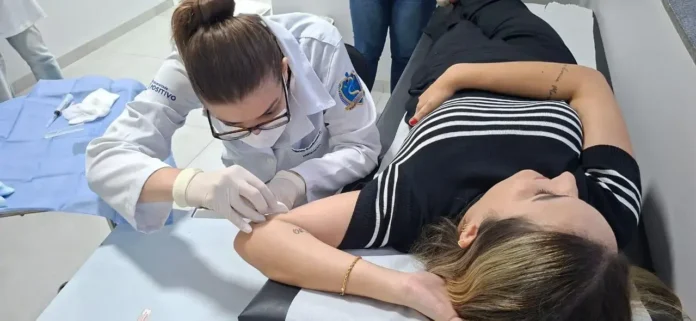 Profissional aplique procedimento em braço de paciente durante consulta em ambiente clínico.