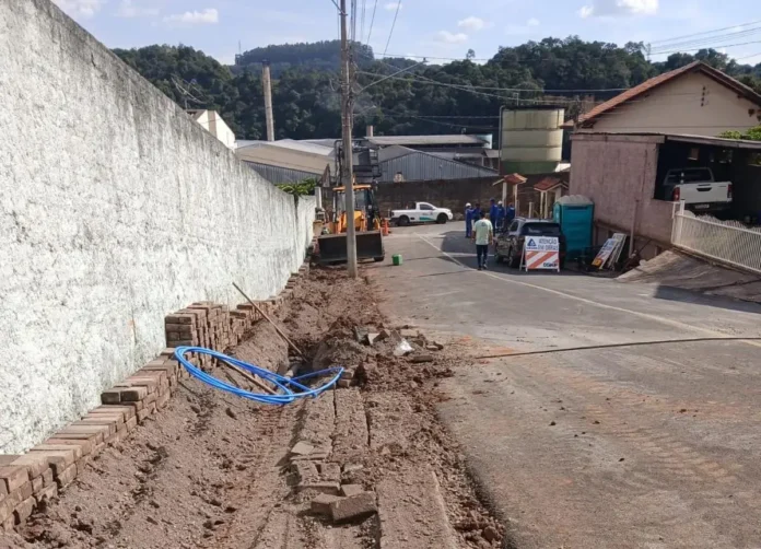 Trabalho de obras em rua, com máquinas, tubos azuis e sinalização de atenção nas proximidades.