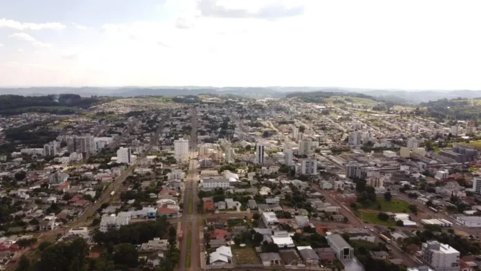 Vista aérea de uma cidade com prédios, ruas e áreas verdes ao fundo.