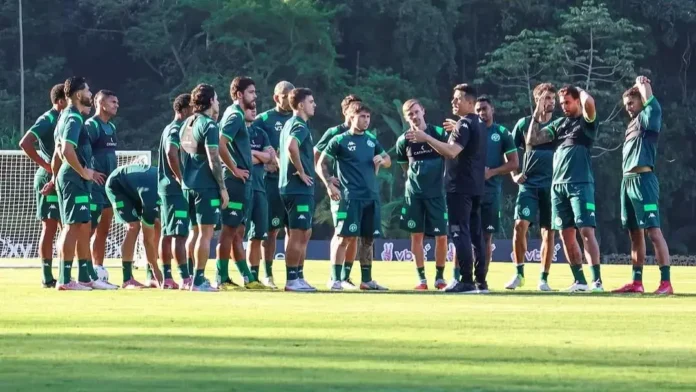 Treinamento de futebol com jogadores em uniforme verde, ouvindo as instruções de um treinador em um campo.