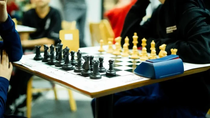 Tabuleiro de xadrez com peças pretas à esquerda e peças brancas à direita, em um ambiente de competição.