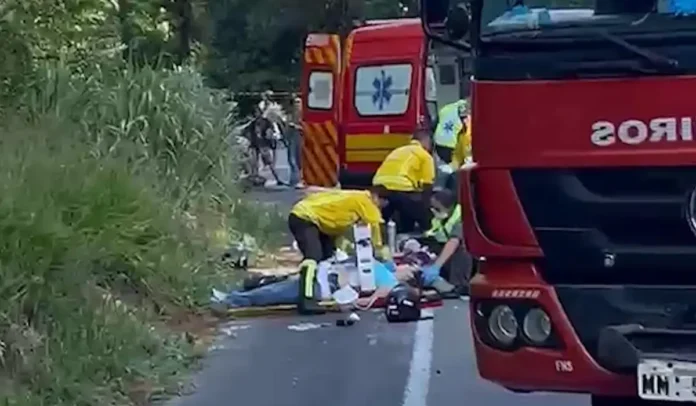 Equipes de emergência prestando socorro a uma vítima em rodovia, com ambulâncias e uma viatura de bombeiros ao fundo.