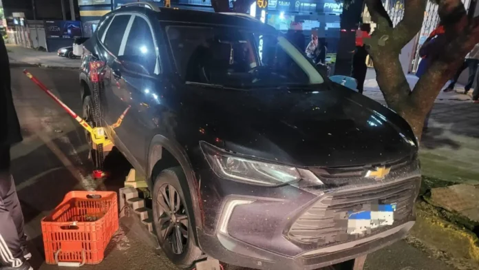 Veículo negro levantado por um macaco hidráulico, com um cesto laranja ao lado em uma via urbana.