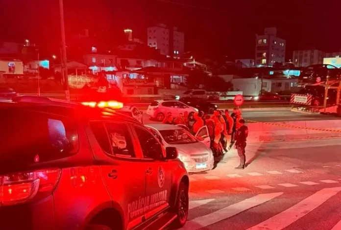 Grupo de policiais próximos a um veículo em área urbana durante a noite, com iluminação vermelha.