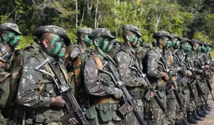 Militares em formação, com camuflagem facial, armados e vestidos com uniformes de combate na floresta.