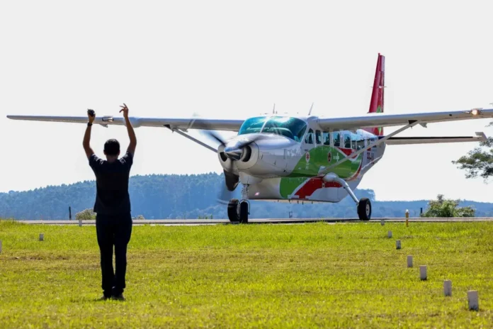 Aeronave de asas fixas se aproxima enquanto um operador sinaliza com as mãos no campo.