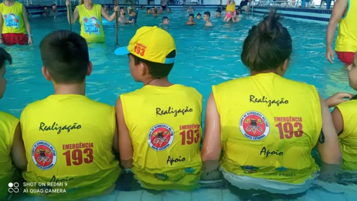 Crianças usando coletes amarelos com inscrições do Projeto Golfinho enquanto estão na piscina.