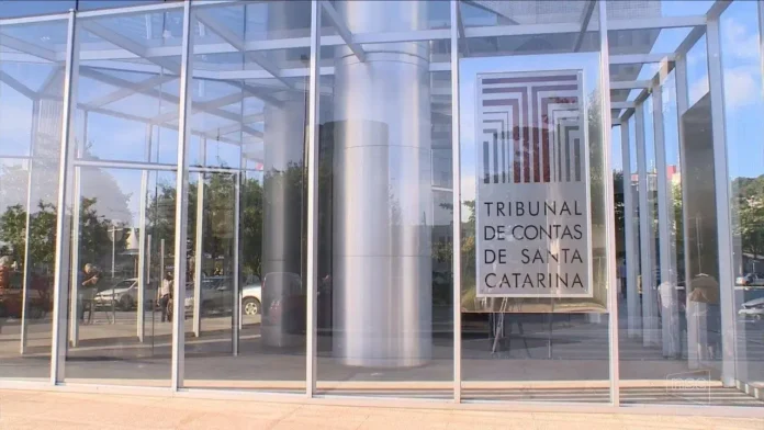Edifício com estrutura de vidro e placa visível com a inscrição "TRIBUNAL DE CONTAS DE SANTA CATARINA".