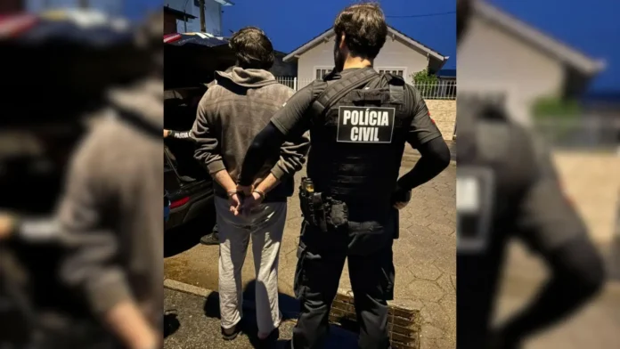 Agente da Polícia Civil com colete, próximo a homem algemado, em área urbana à noite.