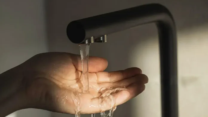 Água escorrendo de uma torneira em uma mão aberta, capturando o líquido.