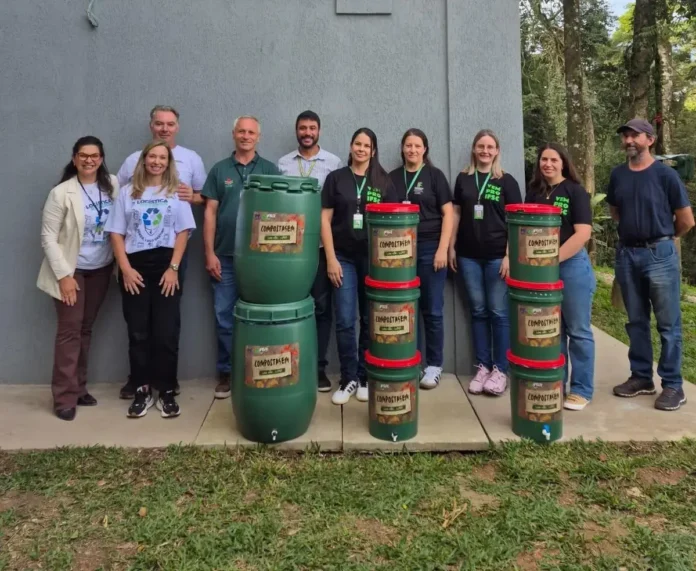 Grupo de pessoas em pé, ao lado de composteiras, em um ambiente externo. Texto visível: "COMPOSTAGEM".