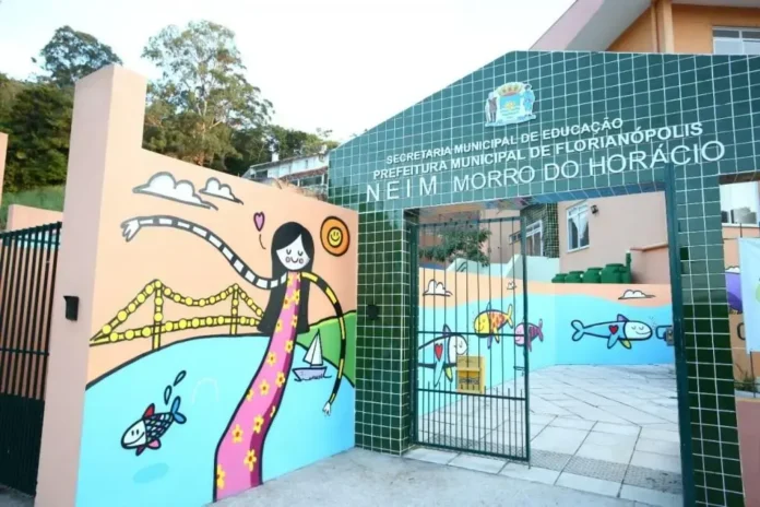 Entrada de uma instituição de educação com mural ilustrativo e informações sobre a Secretaria Municipal de Educação.