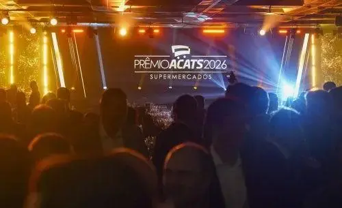 Público reunido em evento com tela ao fundo destacando o Prêmio Acats 2026 Supermercados e luzes decorativas.