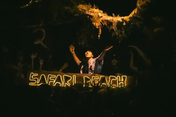 DJ se apresentando no Safari Beach com iluminação em neon, cercado por uma multidão animada.