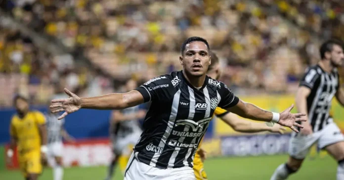 Atleta comemora gol com os braços abertos em um estádio lotado, com torcedores ao fundo.