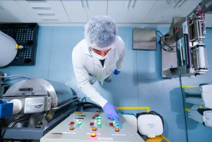 Pessoal em laboratório técnico operando equipamentos em painel de controle com luzes indicativas.