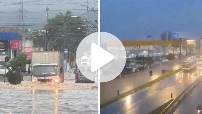 Caminhões e carros enfrentam alagamentos em ruas durante forte chuva, com nível da água elevado.