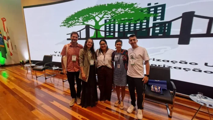 Grupo de pessoas posando em um evento sobre Arborização Urbana, com um banner ao fundo e bandeiras.