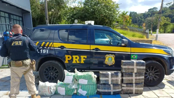 Veículo da PRF estacionado ao lado de pacotes de drogas apreendidos durante uma operação policial.