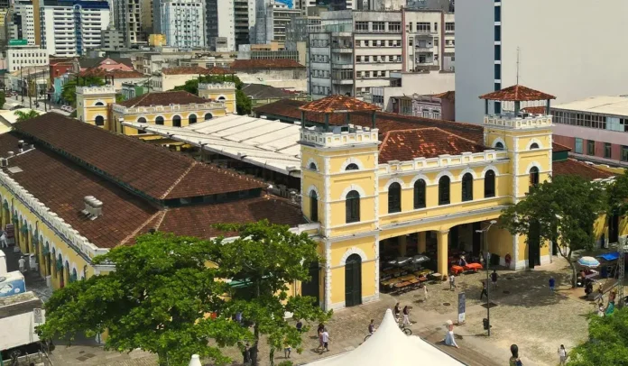 Vista aérea de um prédio amarelo com telhado de cerâmica, cercado por árvores e áreas urbanas.