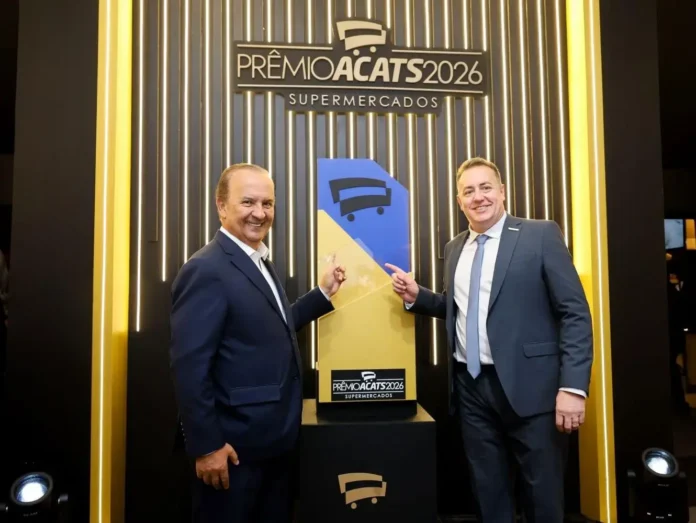 Duas pessoas apontam para o troféu do Prêmio ACATS 2026 em um evento de premiação.