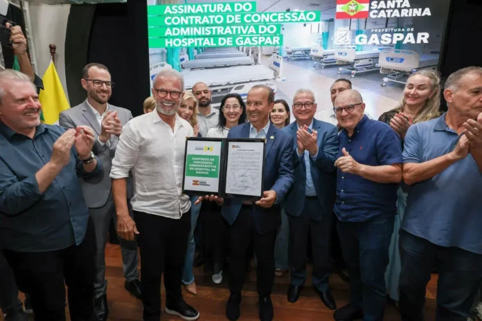 Cerimônia de assinatura do contrato de concessão administrativa do Hospital de Gaspar, com várias pessoas aplaudindo.