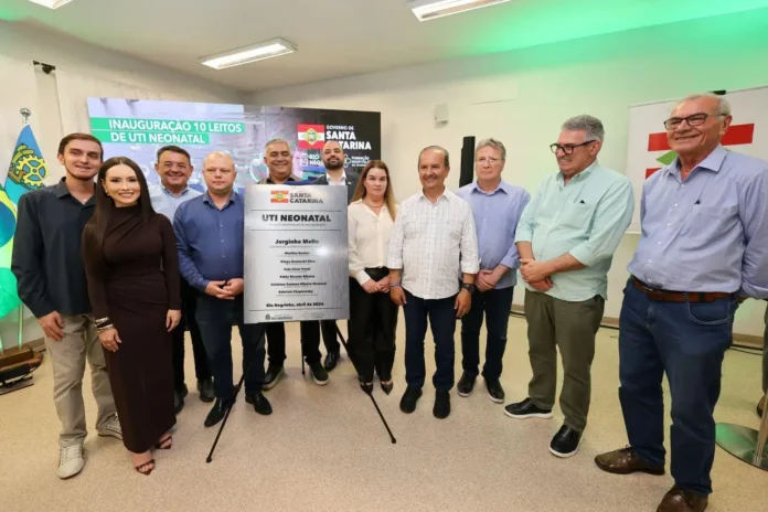 Grupo de pessoas posando em evento de inauguração de 10 leitos de UTI Neonatal, com placa comemorativa ao fundo.