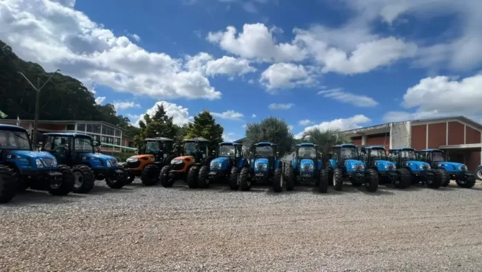 Conjunto de tratores agrícolas estacionados em um espaço aberto com céu azul e algumas nuvens ao fundo.