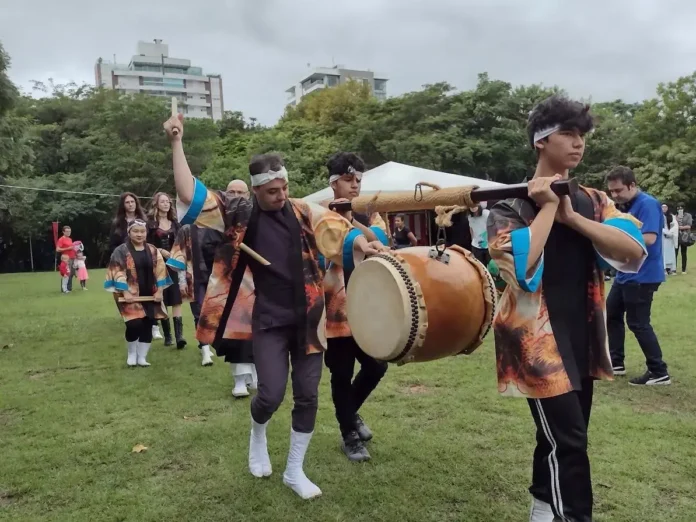 Grupo de pessoas vestindo roupas tradicionais, apresentando uma performance com tambores em um parque.