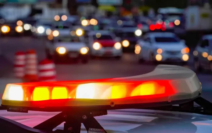 Sinalização luminosa de um veículo de emergência em primeiro plano, enquanto carros em movimento são visíveis ao fundo em via pública.